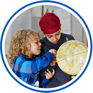 Two elementary students pointing at a globe in a classroom.