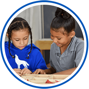 Two elementary students doing an activity at a desk in their classroom.
