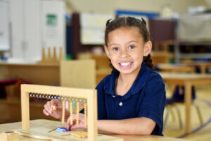 Battle Creek Montessori Academy smiles at her desk while she uses Montessori Method tools in the classroom.